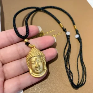 Gold Buddha head copper pendant necklace with black woven rope and white bead accents, close-up handheld view