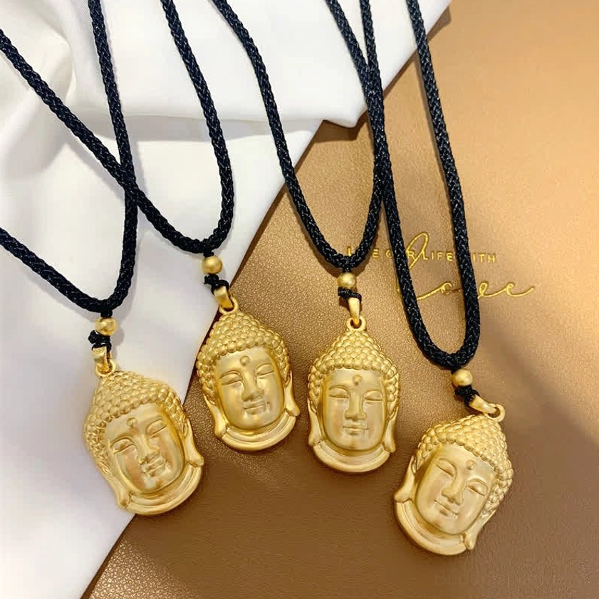 Four gold Buddha head pendants in two different sizes with black hanging ropes, top-down flat lay composition