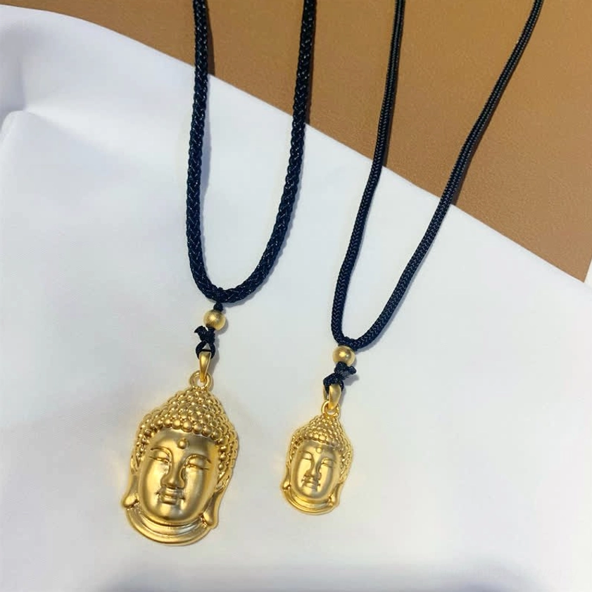 Two pairs of gold Buddha head pendants in different sizes on black hanging cords, flat lay arrangement