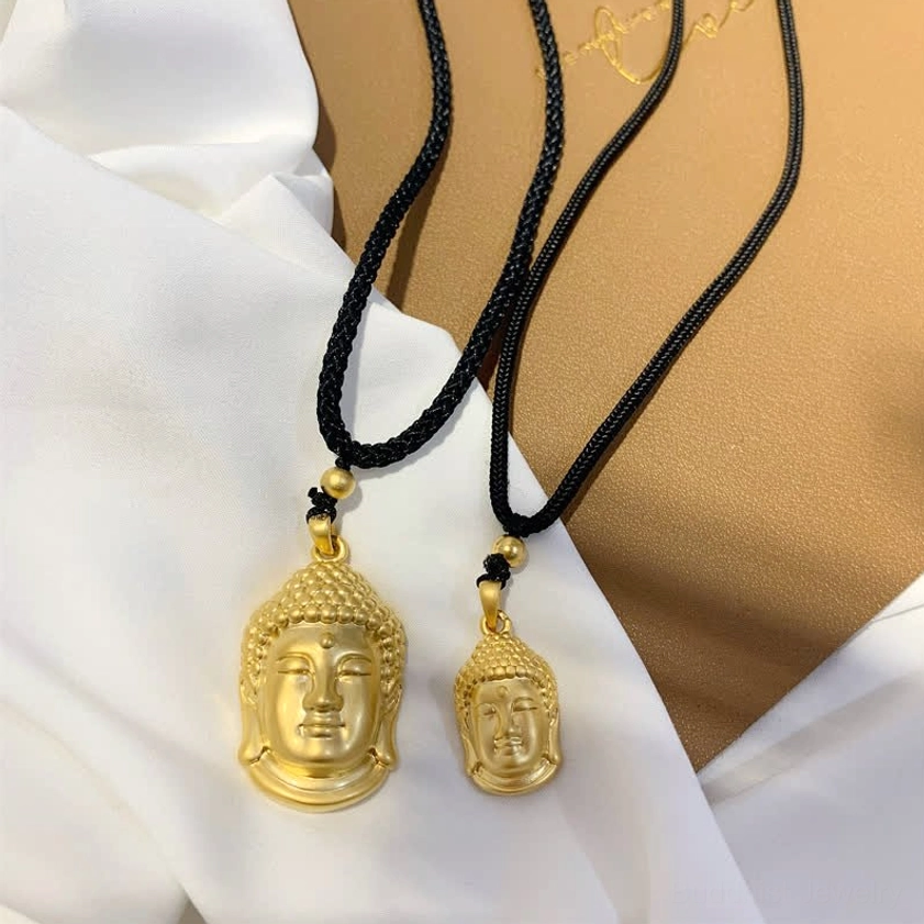 Large and small gold Buddha head pendant necklaces with black cords arranged in flat lay composition