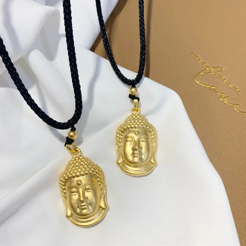 Two sizes of gold Buddha head pendant necklaces displayed flat lay, showing small and large copper pendants on black braided cords