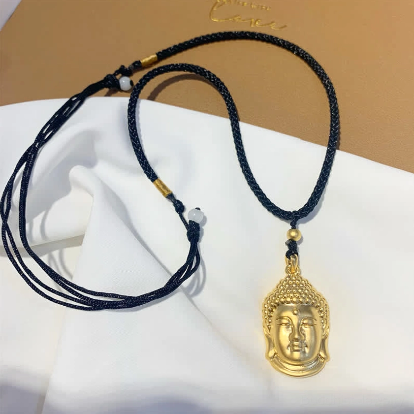 Single gold Buddha head copper pendant necklace with adjustable black rope, top-down flat lay display