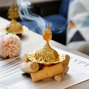 Gold Buddhist incense burner with smoking incense cone and wooden coaster on home table with flowers - top three-quarter view