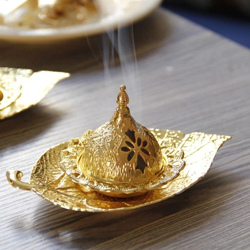 Gold incense burner set overhead view with rising smoke from incense cone, ornate carved lid and leaf tray