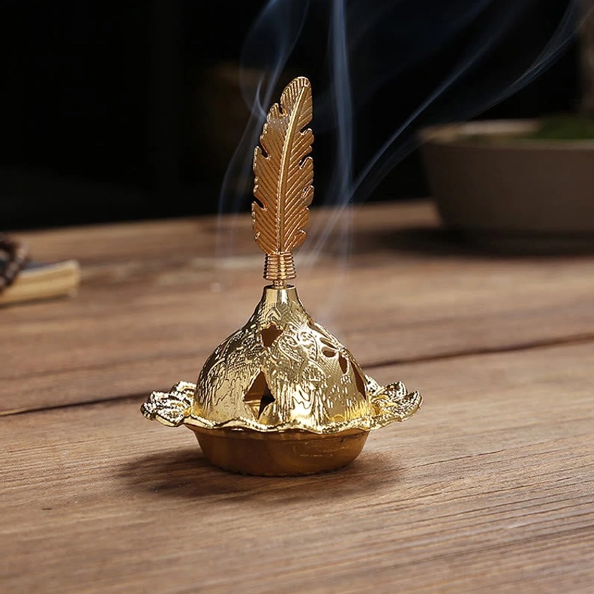 Gold feather incense burner with pointed finial design and intricate carved details on wooden surface