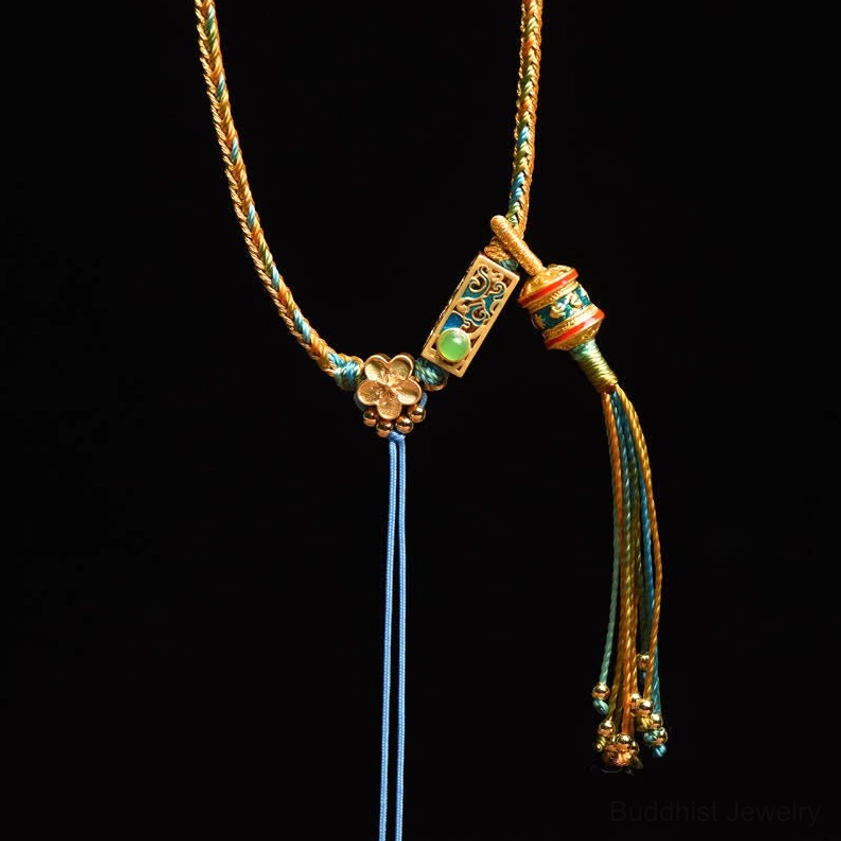 Gold and green braided copper Buddhist necklace with blue tassel and flower-shaped enamel charm on black background