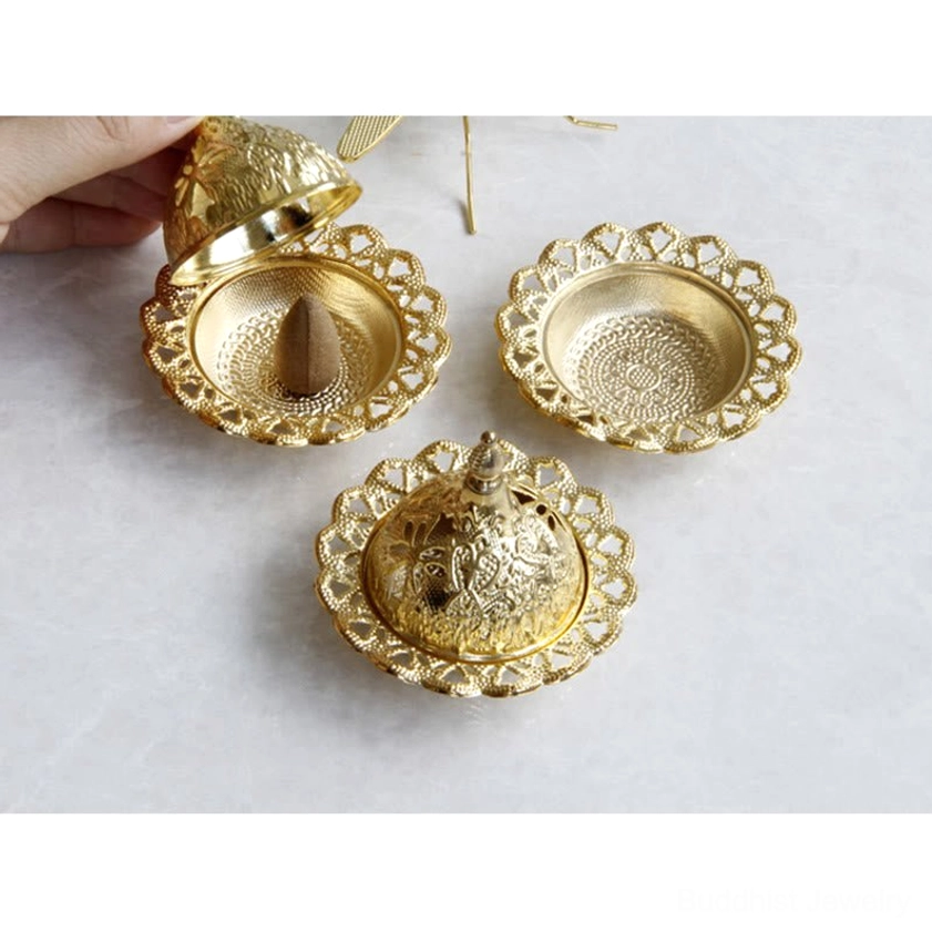 Human hand opening gold Buddhist incense holder lid with cone incense and lace-hollowed tray visible