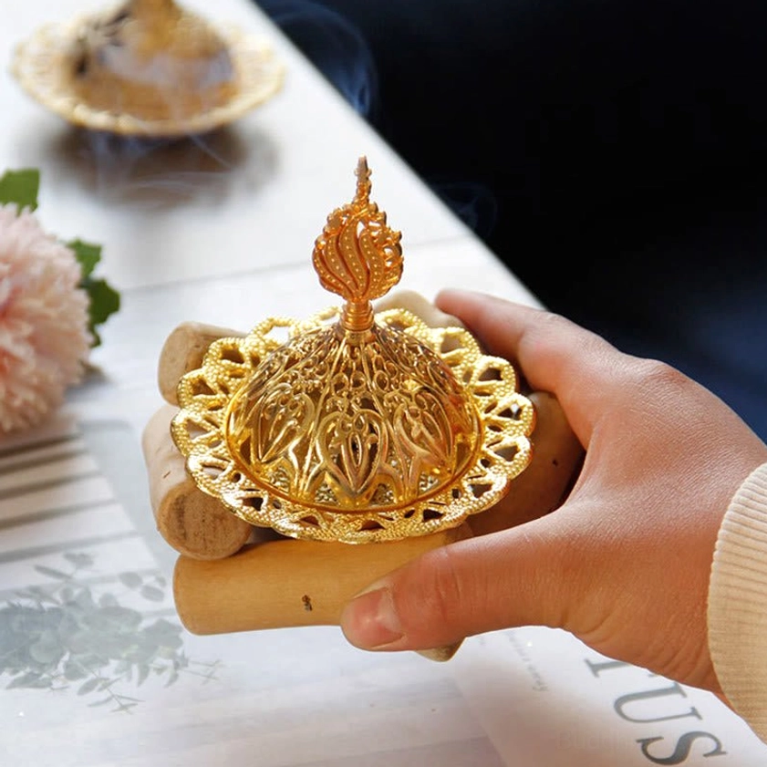 Handheld gold Buddhist incense burner close-up showing hollow carved metal design with wooden base in hand