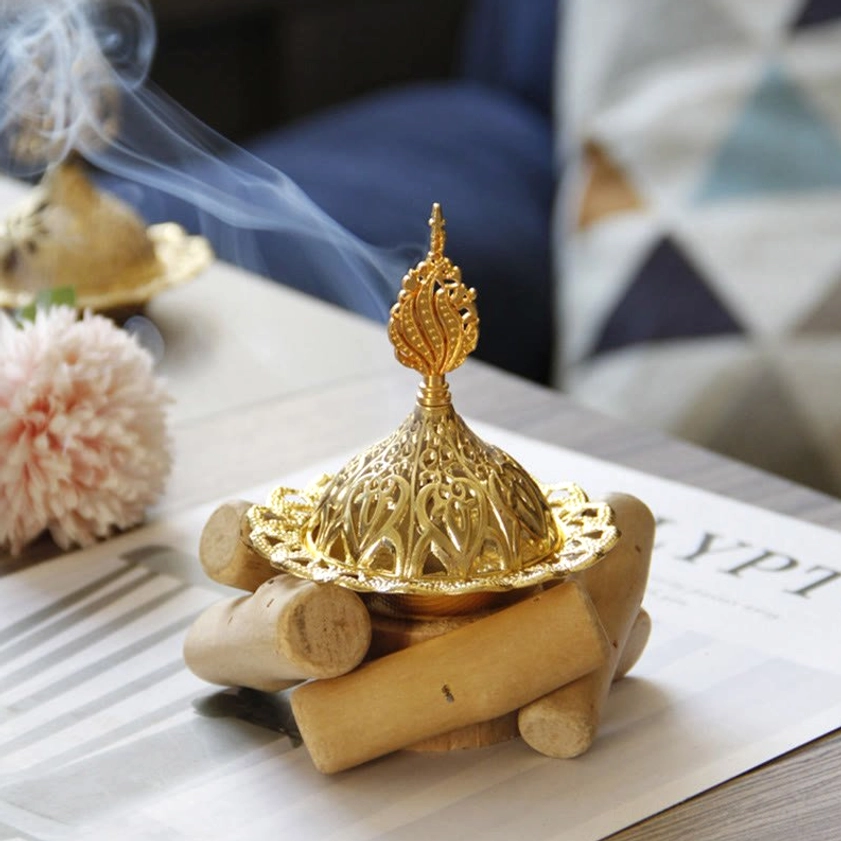 Burning gold Buddhist incense burner with ornate hollow metal lid and smoking incense - front three-quarter view