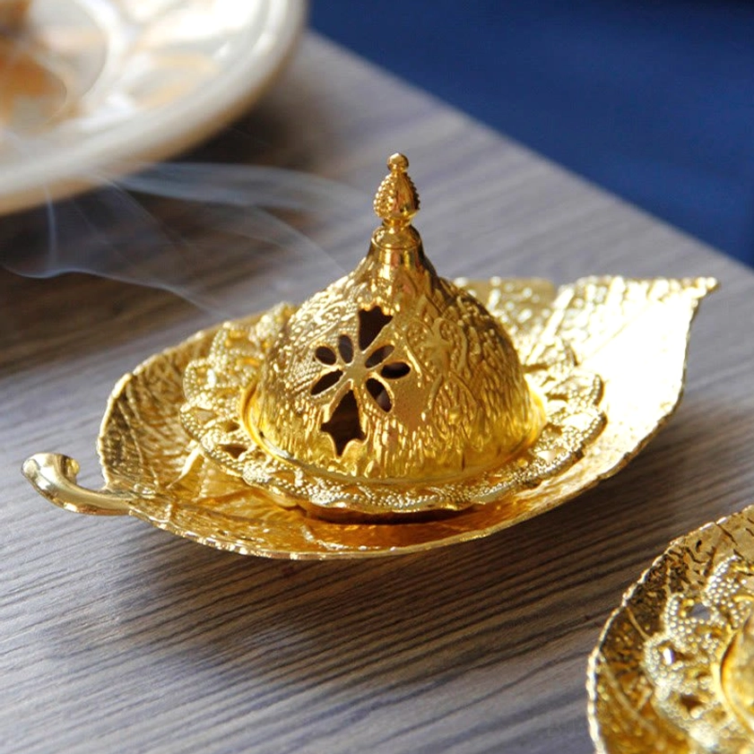 Gold incense burner coaster overhead view with smoking incense, floral hollow design and glowing golden finish