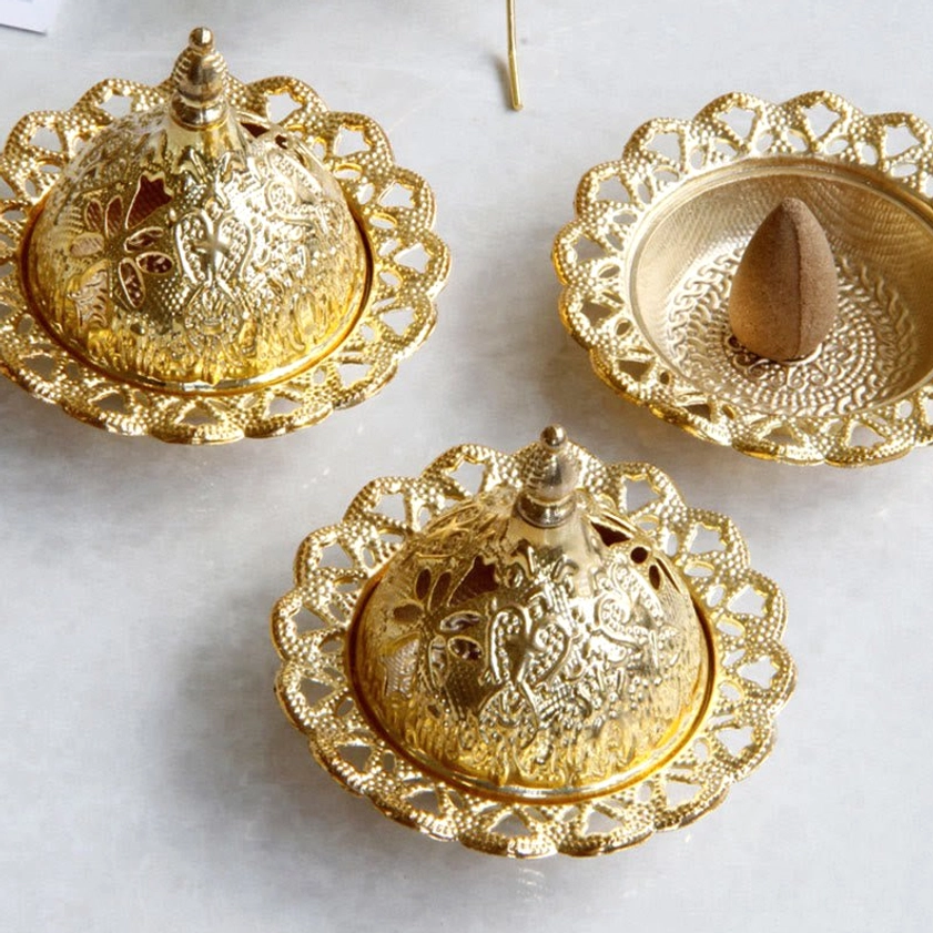 Set of three gold Buddhist meditation incense burners with one displaying cone incense and carved decorative lids