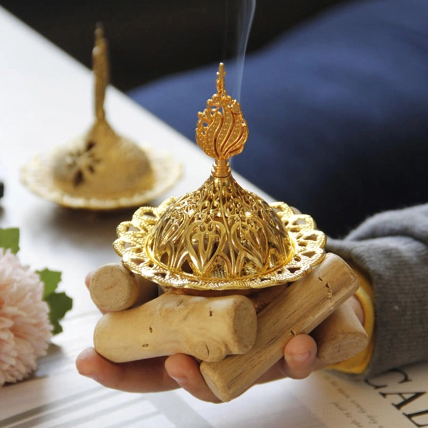 Person holding smoking gold incense burner with ornate hollow carved lid and wooden base - close-up side angle