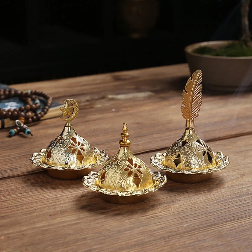 Handcrafted gold incense holder with decorative finials and prayer beads on wooden table