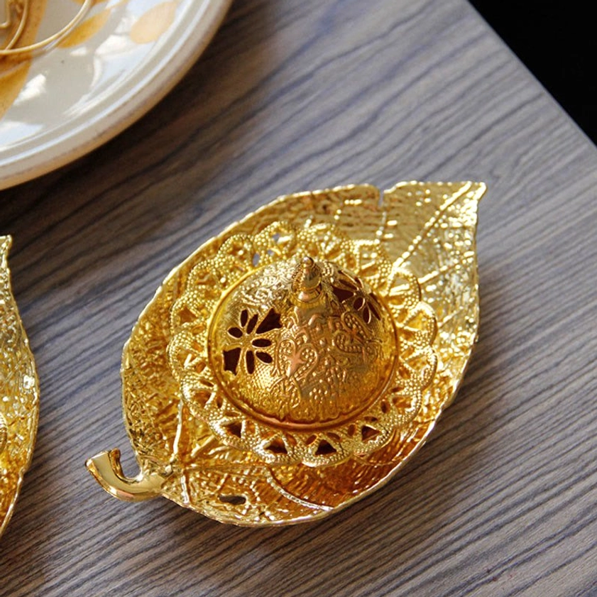 Gold leaf incense burner close-up showing embossed leaf veins and carved decorative rim on wooden surface