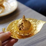 Gold leaf incense burner held by hand, showing intricate carved hollow lid and embossed metal texture on wooden table