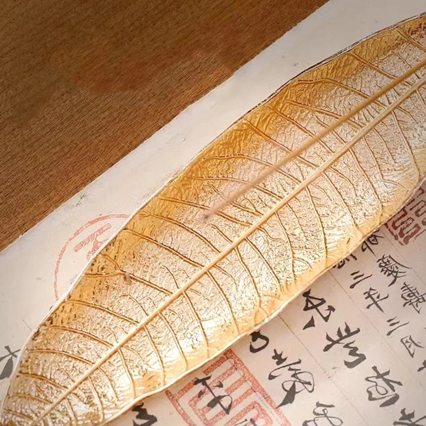 Gold tone Buddhist leaf incense burner with detailed veins displayed on Chinese calligraphy paper