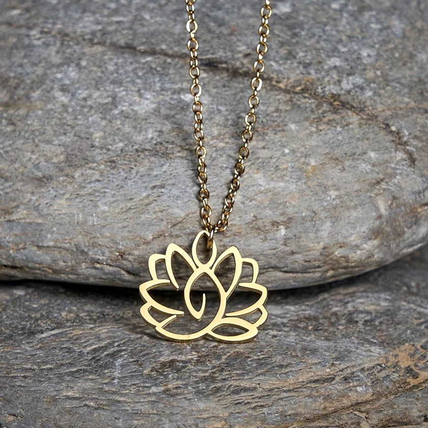 Gold lotus pendant necklace in oblique overhead view on natural stone backdrop, thin gold chain with hollow carved lotus shape