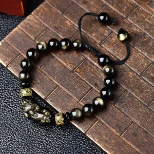 Gold sheen obsidian Pixiu bracelet with Om Mani Padme Hum beads on wooden background, showing glossy golden-black obsidian beads and black adjustable braided cord