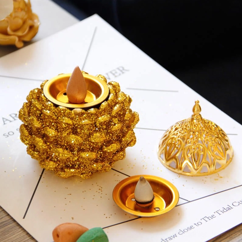 Gold pine cone incense burner with backflow incense cones and decorative props on tabletop display