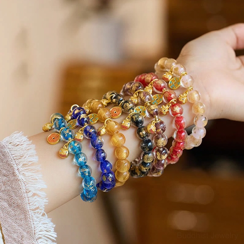 Stacked Buddhist prosperity bracelets featuring gold swallowing beast charms and gradient colored glass beads