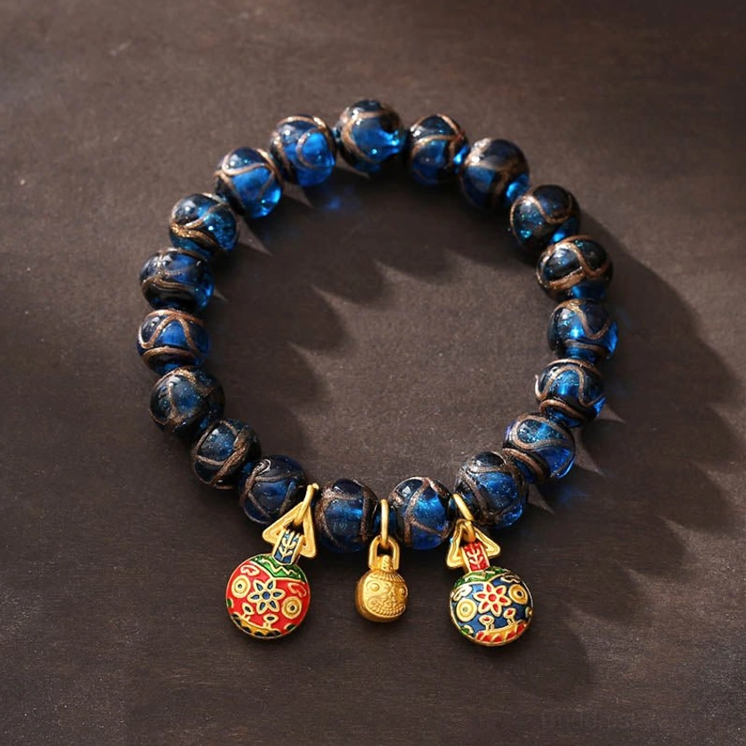 Gold Pixiu wealth bracelet with blue liuli glass beads and three protective prosperity charms - overhead view