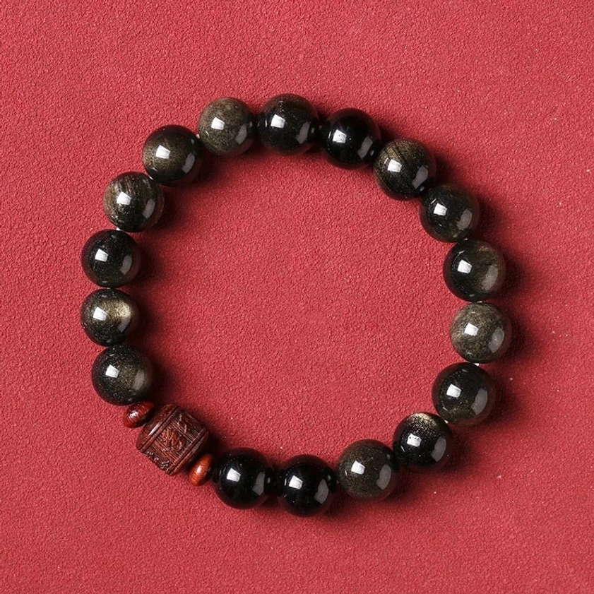 Gold Sheen Obsidian beads with carved reddish-brown focal bead and red spacers on solid matte red background, flat lay