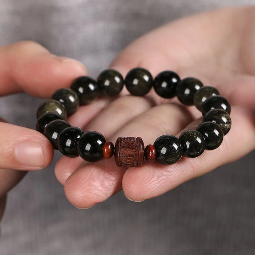 Close-up of gold sheen obsidian bracelet held in hand, showing smooth polished black beads with golden flecks and carved detail bead