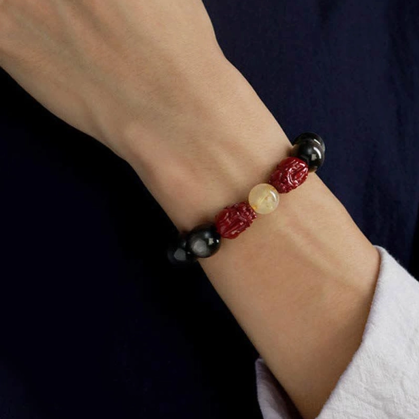 Gold sheen obsidian Buddhist protection bracelet worn on wrist showing black beads and red cinnabar pixiu