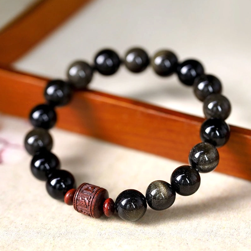 Gold Sheen Obsidian bracelet with Om Mani Padme Hum engraving on wooden tray, showing golden shimmer and reddish-brown focal bead