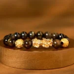 Gold sheen obsidian Pixiu wealth bracelet overhead flat lay with dark obsidian beads and gold-plated charm on wooden display