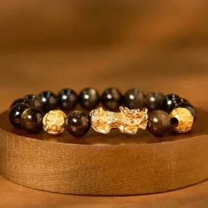 Gold sheen obsidian Pixiu wealth bracelet overhead flat lay with dark obsidian beads and gold-plated charm on wooden display