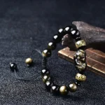 Gold Sheen Obsidian Pixiu Om Mani Padme Hum Buddhist protection bracelet, oblique overhead view showcasing black and gold tones with adjustable rope cord