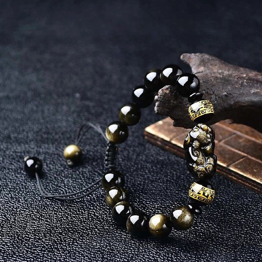 Gold Sheen Obsidian Pixiu Om Mani Padme Hum Buddhist protection bracelet, oblique overhead view showcasing black and gold tones with adjustable rope cord