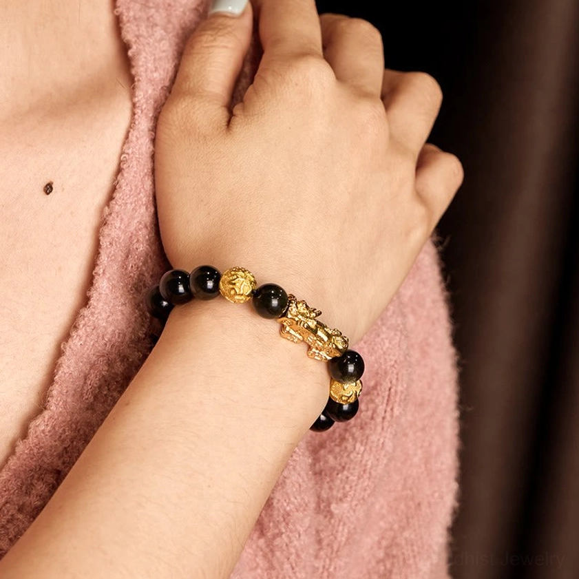 Gold sheen obsidian Pixiu bracelet worn on wrist against soft pink fabric background, showing how the Buddhist wealth bracelet fits naturally on the hand