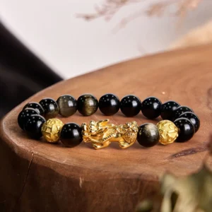 Gold sheen obsidian Pixiu wealth bracelet with Om Mani Padme Hum charm displayed on wooden stump, showcasing jet black beads with golden luminescence and gold-plated accents
