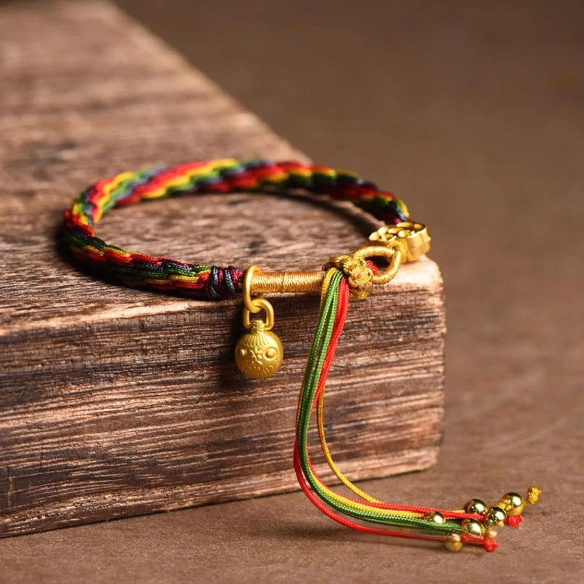 Minimalist gold swallowing beast baby bracelet with colorful braided cord and round enamel charm detail on wooden background