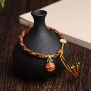 Gold Swallowing Beast Mother blessed string bracelet with colorful braided cord, gold charm, and tassel bells on wooden surface