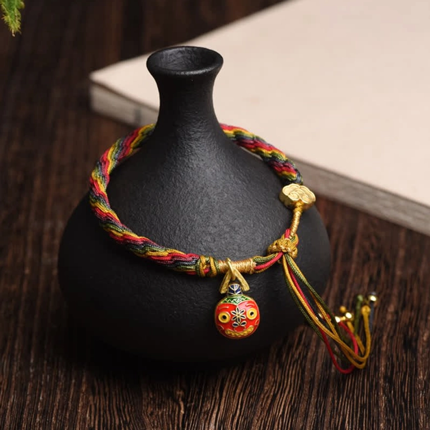 Gold Swallowing Beast Mother blessed string bracelet with colorful braided cord, gold charm, and tassel bells on wooden surface