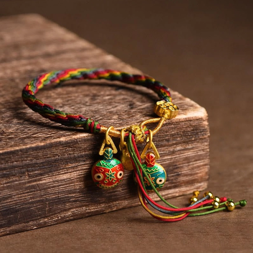 Gold swallowing beast braided string bracelet side view showing multi-color woven cord with enamel pendant and gold tassel accents