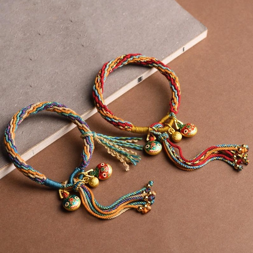 Gold swallowing beast family fortune braided string bracelet with multicolor enamel charms and tassel, displayed on brown paper with top-down view