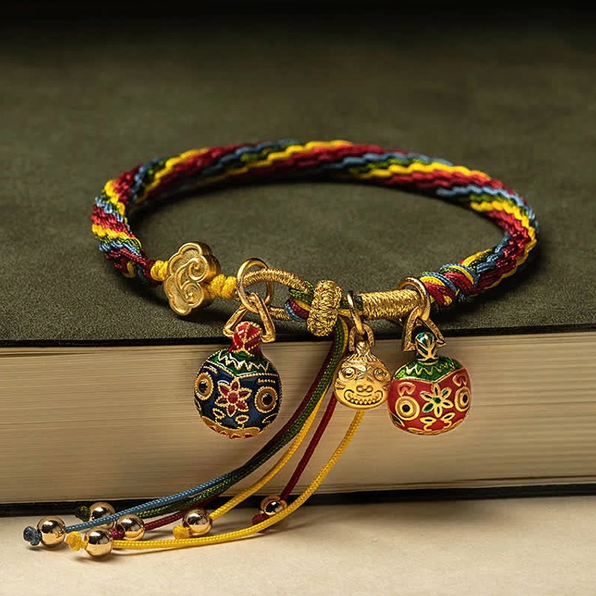 Gold Swallowing Beast Family bracelet with multiple enamel charms and tassel bells on book surface