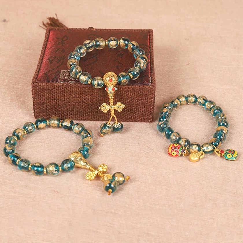 Gold Swallowing Beast Vajra Buddhist bracelet set with teal beads and gold enamel charms, displayed with gift box and flat lay styling