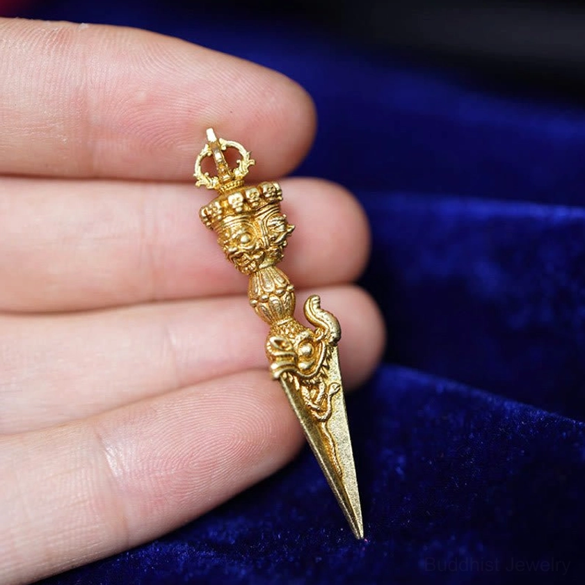 Gold vajra ritual dagger pendant with detailed religious motifs on velvet background