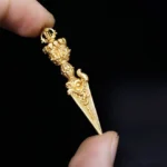 Gold vajra dorje pendant handcrafted with intricate carved details held in hand close-up view