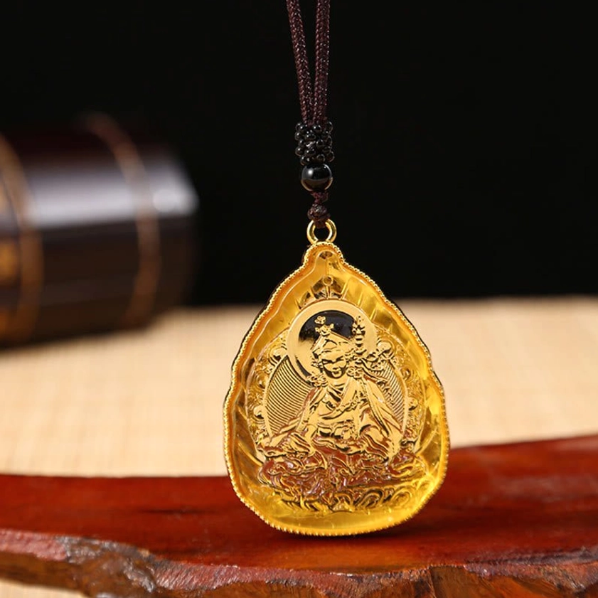 Golden Buddhist Buddha crystal pendant necklace on beaded black cord displayed on red wooden base with detailed Buddha engraving and gold metal rim visible
