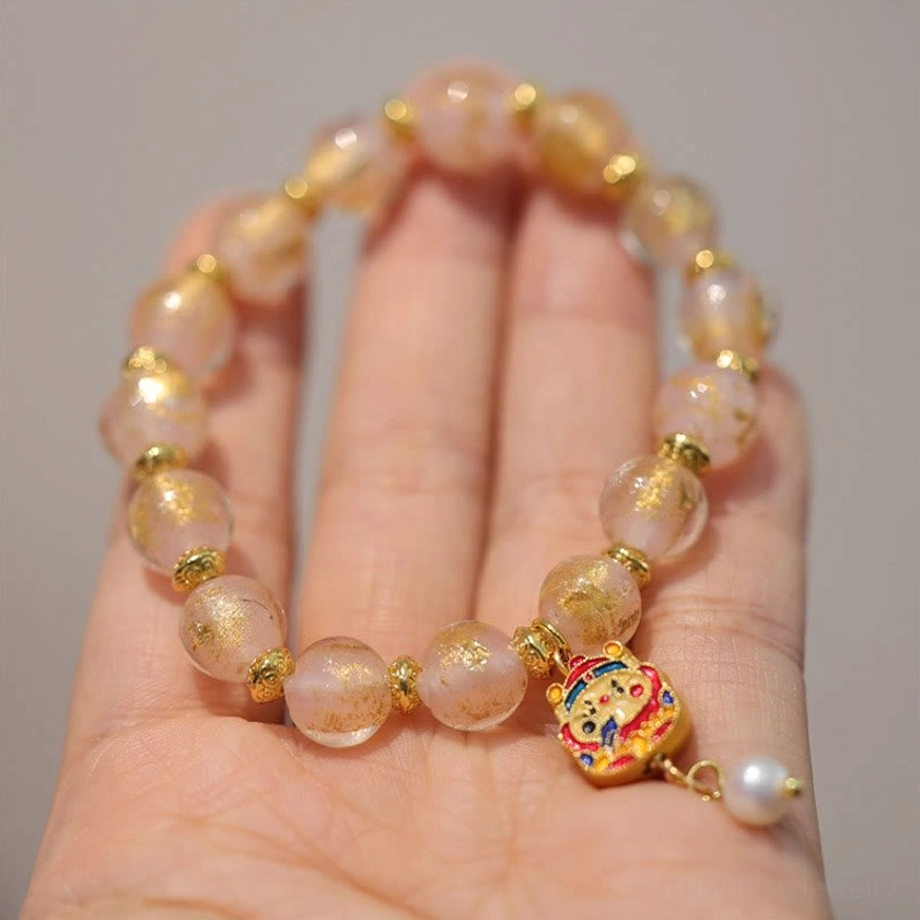 Golden bead God of Wealth charm bracelet worn on wrist with red beads, gold spacers, and green gemstone gourd pendant
