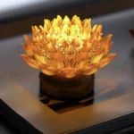 Golden lotus liuli glass illuminated sculpture with copper brass base on book, warm ambient lighting, top view showing petal details