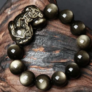 Golden Obsidian Pixiu Wealth Protection Bracelet with glossy beads and carved metal charm on wooden background