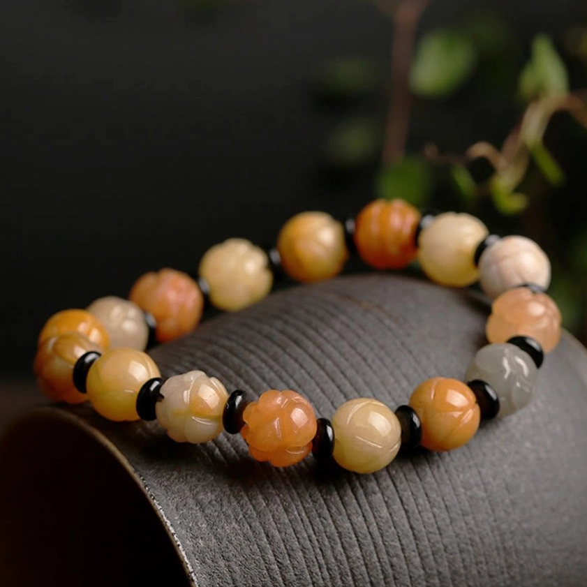 Close-up detail of Golden Silk Jade Lotus Buddhist bracelet on dark fabric base highlighting carved floral bead patterns and black spacer beads