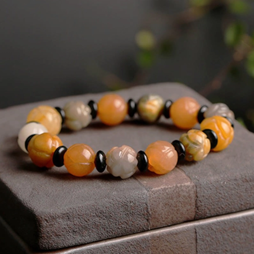 Golden Silk Jade Lotus Bracelet on dark stone base showing natural bead color variations and black spacer details